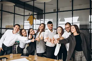 A group of smiling business people giving a thumbs up in an office setting.
